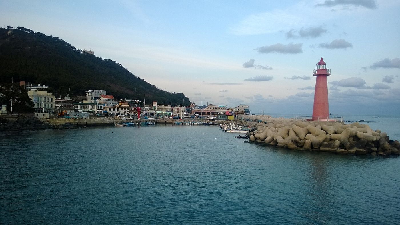 맑은 날 청사포의 붉은 등대와 테트라포드 방파제, 그 곁의 어촌 포구