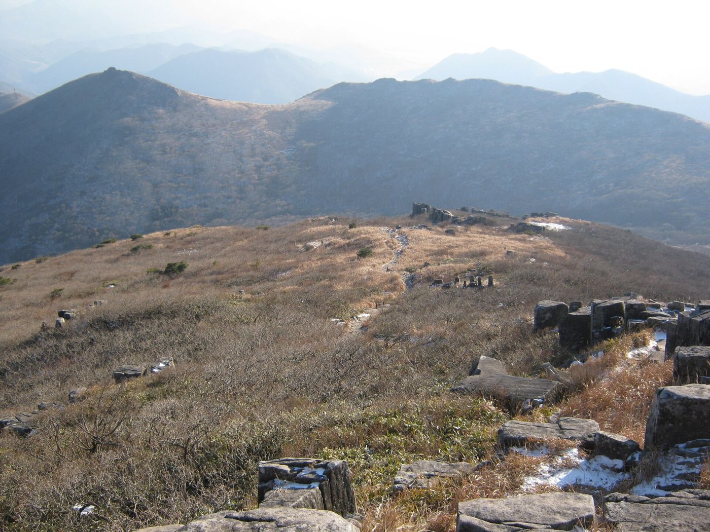 무등산 능선의 주상절리와 마른 억새 — 겹겹의 산줄기가 뒤로 펼쳐진다
