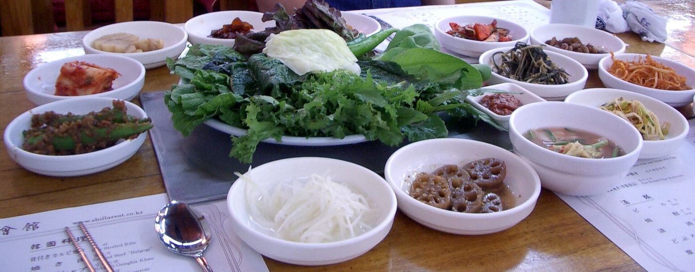 경주 쌈밥 한 상 — 가운데 쌈채소 한 접시를 두고 둘레로 강된장·나물·김치·조림이 그릇그릇 따라 나온다