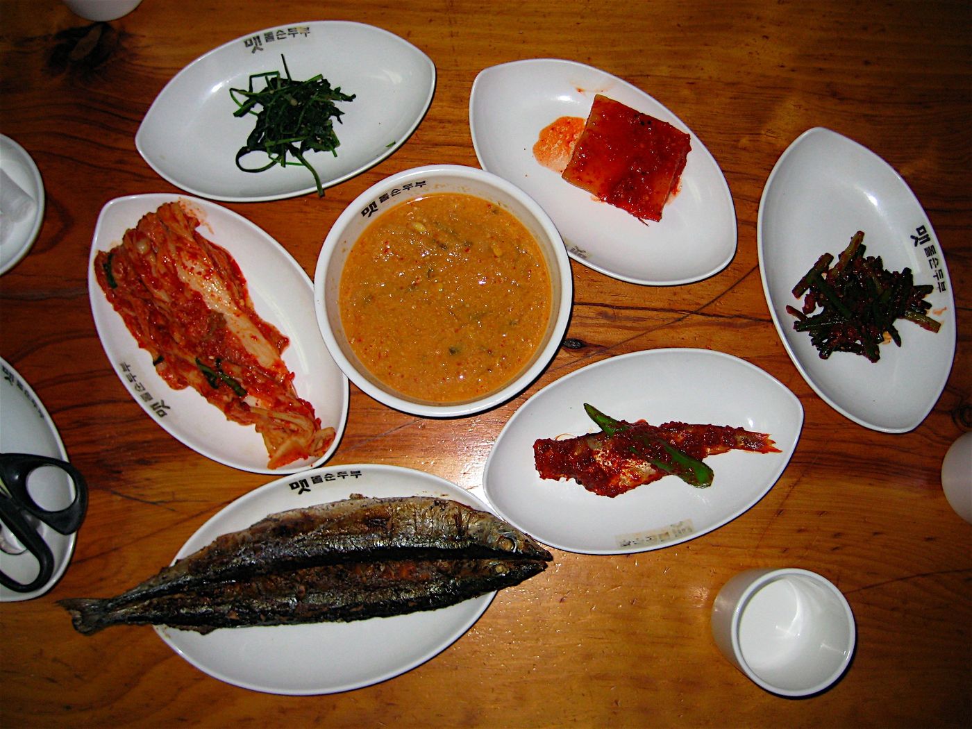 경주 한식 백반상 — 나무 상에 생선구이와 배추김치, 강된장, 나물무침 등 반찬이 여러 접시 깔렸다