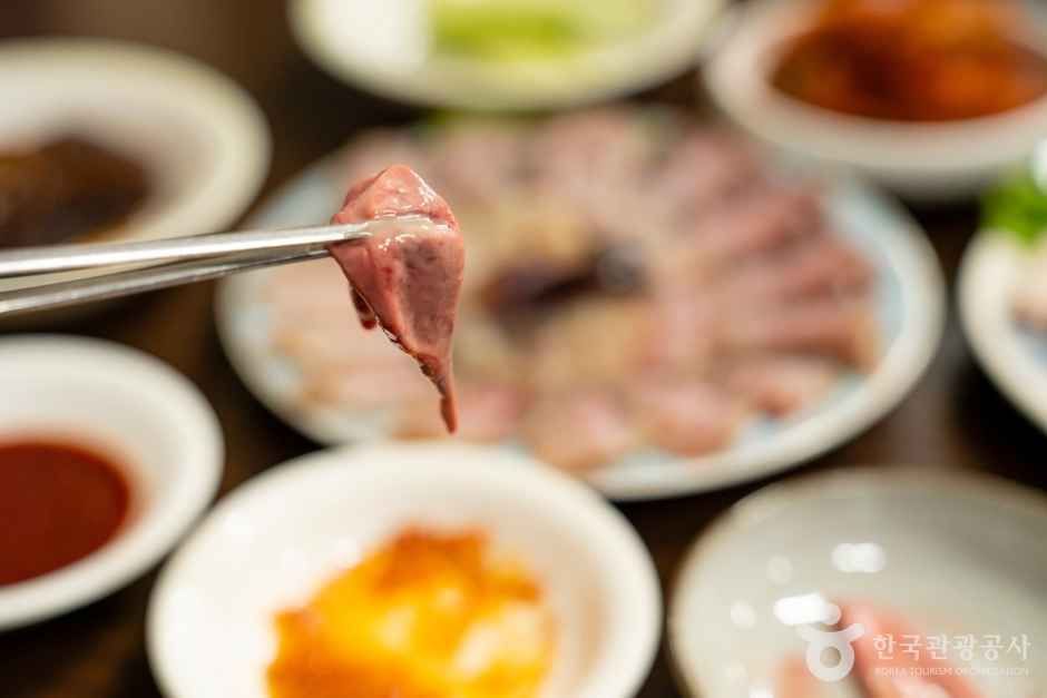 젓가락에 집어 든 홍어삼합 한 점 — 삭힌 홍어에 수육과 묵은지를 곁들이는 남도의 대표 별미