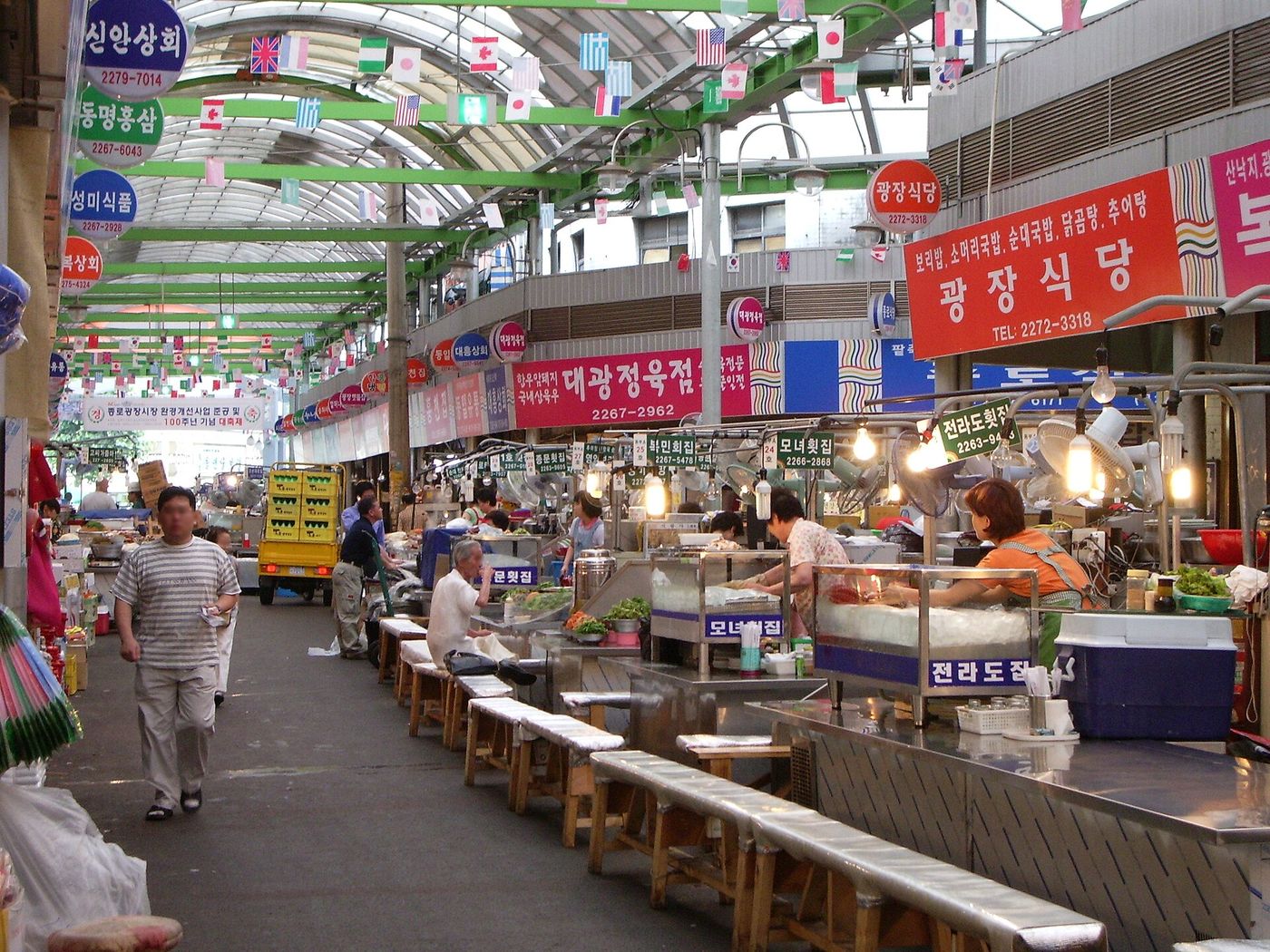 광장식당·회집 간판이 늘어선 광장시장 먹자골목 — 좌판 사이로 사람들이 오간다