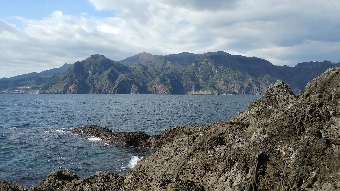 바위 해안 너머로 바라본 울릉도 산줄기 — 일주도로에서는 바다와 화산 능선이 번갈아 펼쳐진다